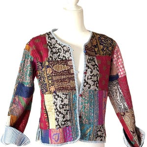 May include: A patchwork jacket with a variety of colorful fabric patterns. The jacket features a round neckline, long sleeves with striped cuffs, and a button closure. The jacket is displayed on a mannequin.