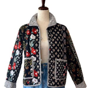 May include: A quilted jacket with a floral pattern in red, white, and green on a black background. The jacket has a striped collar and cuffs, with white trim and two pockets. The jacket is displayed on a mannequin.