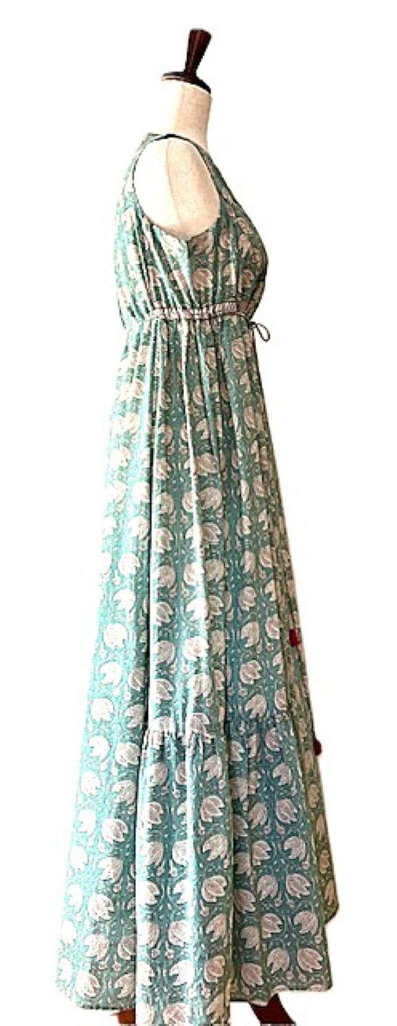 Puede incluir: Un vestido largo de maxi azul verdoso con estampado floral blanco. El vestido tiene una cintura fruncida y una falda de capas.