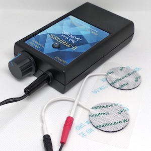 May include: Black E-Trifier Bob Beck Zapper device with a blue and white geometric design on the top. It has a knob for intensity and two electrode pads connected by wires. The text "E-TRIFIER Bob Beck ZAPPER" is visible.