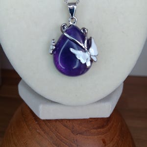 May include: A silver necklace with a teardrop-shaped amethyst pendant and a white butterfly charm.