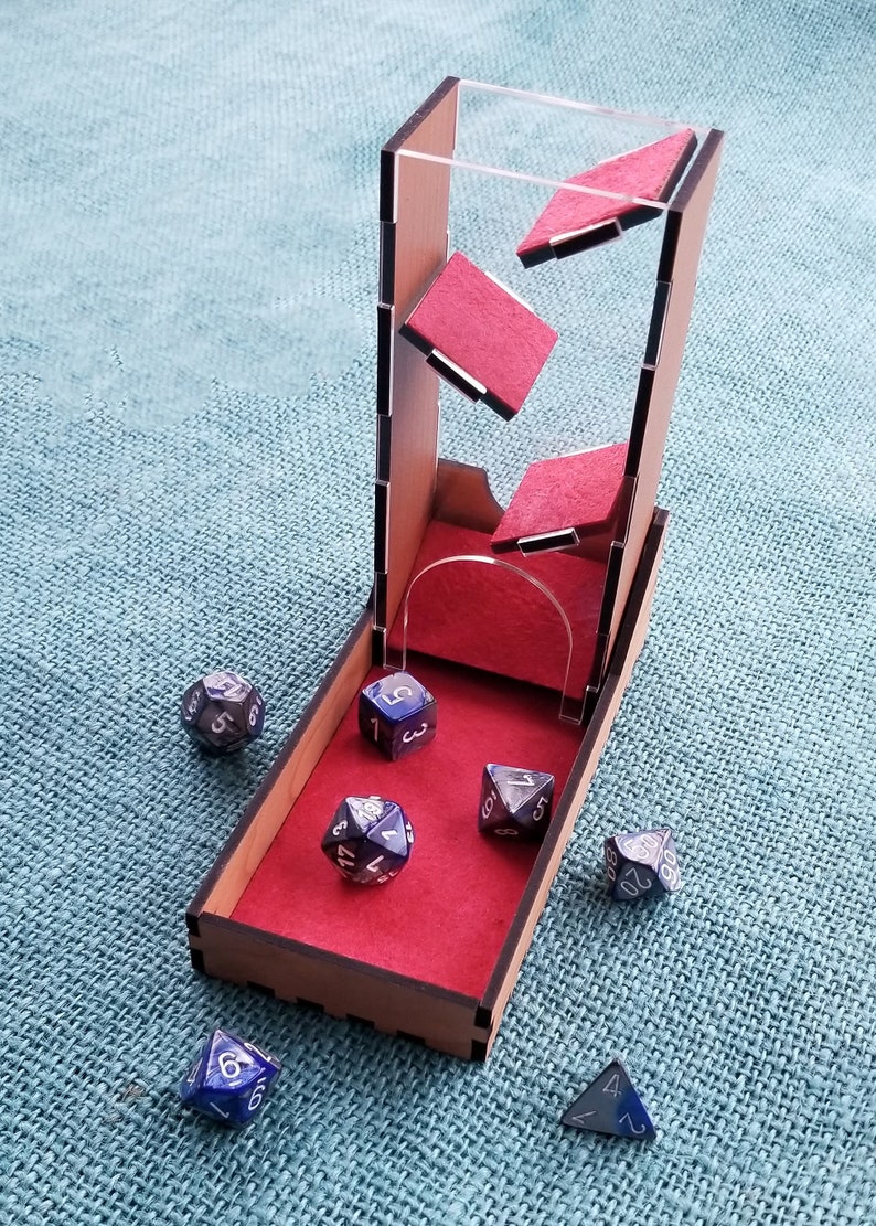 May include: A wooden dice tower with a clear acrylic top and red felt lining. The tower has a slot for dice to fall through and a red felt tray at the bottom. There are six blue and silver dice scattered around the tower.