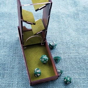 May include: A wooden dice tower with a green felt interior and a clear acrylic top. The tower is open and several green dice with white numbers are scattered around it.