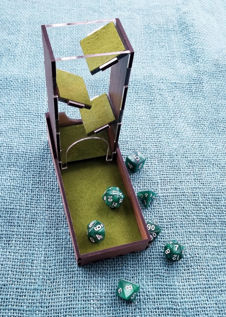 May include: A wooden dice tower with a green felt interior and a clear acrylic top. The tower is open and several green dice with white numbers are scattered around it.