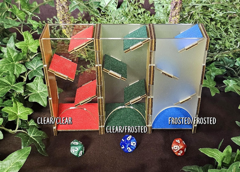 May include: Three clear acrylic dice towers with different frosted glass panels. The towers are labeled "CLEAR/CLEAR", "CLEAR/FROSTED", and "FROSTED/FROSTED".  Each tower has a different colored felt base: red, green, and blue.
