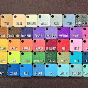 May include: A color chart with 36 small squares of felt fabric, each labeled with a color name. The colors include gold, tan, beige, eggshell, white, gray, steel, charcoal, black, brown, chocolate, eggplant, purple, lavender, amethyst, violet, magenta, mustard, honey, orange, salmon, burgundy, red, pink, rose, yellow, lime, green, emerald, forest, moss, teal, dark teal, navy, cobalt, blue, ocean, sky, arctic, sapphire, and turquoise.