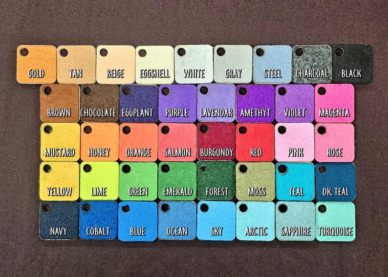 May include: A color chart with 36 small squares of felt fabric, each labeled with a color name. The colors include gold, tan, beige, eggshell, white, gray, steel, charcoal, black, brown, chocolate, eggplant, purple, lavender, amethyst, violet, magenta, mustard, honey, orange, salmon, burgundy, red, pink, rose, yellow, lime, green, emerald, forest, moss, teal, dark teal, navy, cobalt, blue, ocean, sky, arctic, sapphire, and turquoise.