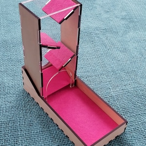 May include: A wooden dice tower with a clear acrylic top and pink felt lining. The tower has a series of angled compartments for the dice to roll through.