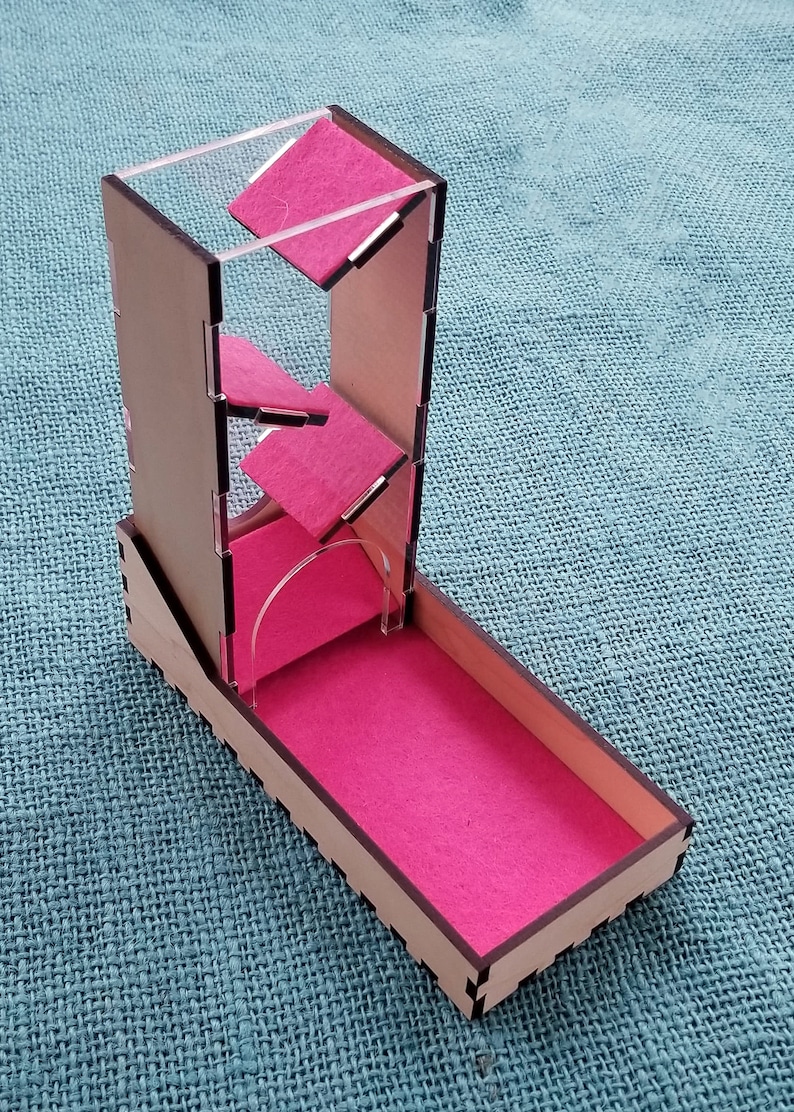 May include: A wooden dice tower with a clear acrylic top and pink felt lining. The tower has a series of angled compartments for the dice to roll through.