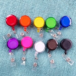 May include: Assortment of 10 colorful retractable badge holders with clear plastic straps. The holders are round and come in red, orange, yellow, green, blue, purple, pink, white, brown, and black.