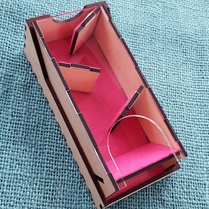 May include: A wooden box with a clear acrylic lid and pink felt lining. The box has a maze-like design with multiple compartments.