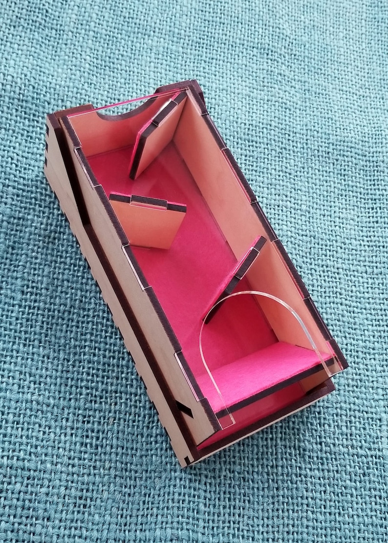 May include: A wooden box with a clear acrylic lid and pink felt lining. The box has a maze-like design with multiple compartments.