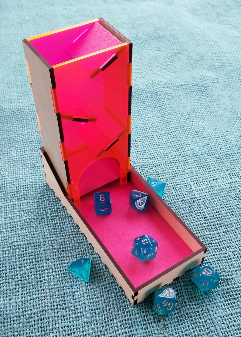May include: A wooden dice tower with a pink acrylic insert and a pink tray. The tower has a slot for dice to fall through. There are six blue dice with gold numbers on a pink tray. The dice are a d4, d6, d8, d10, d12, and d20.