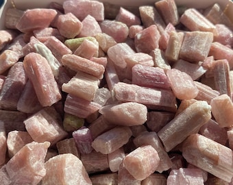 May include: A close-up of a box filled with pink and white tourmaline crystal points. The crystals are various sizes and shapes, and they are all very shiny.