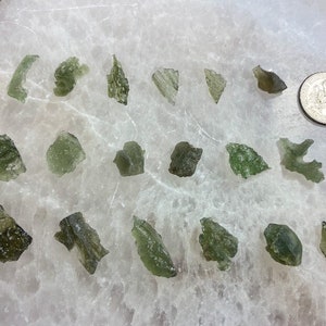 May include: A collection of 18 green aventurine crystals of varying sizes and shapes. The crystals are arranged in three rows labelled A, B, and C. A UK 20 pence coin is included for scale.