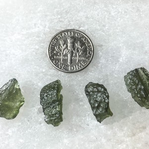 May include: Four green tektite stones, each about the size of a ten pence piece, on a white surface.