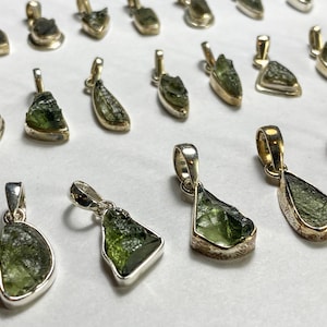 May include: A collection of green peridot gemstone pendants set in silver. The pendants are various shapes and sizes, and some have a rough, natural look.