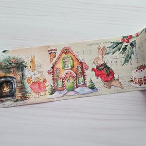 May include: Decorative washi tape featuring a whimsical Christmas scene. The tape showcases illustrations of rabbits, a gingerbread house, a fireplace, and festive elements. The background has musical notes and the text "CHRISTMAS COMES AGAIN".