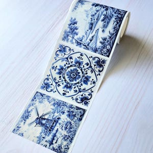 May include: A roll of decorative paper featuring blue and white illustrations. The designs include a landscape scene, a floral pattern, and a windmill. The paper is on a white wooden surface.