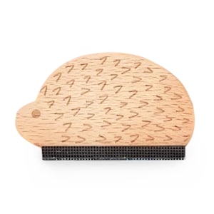 May include: A wooden lint brush shaped like a hedgehog with a black bristle brush on the bottom. The hedgehog is covered in a pattern of small arrows.