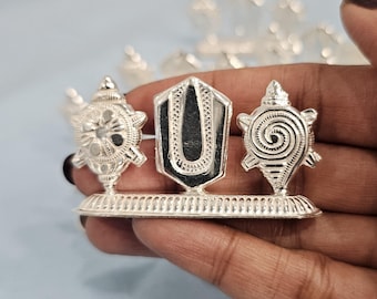 May include: Silver-toned decorative stand with three charms. The charms are a stylized shell, a stylized Om symbol, and a stylized turtle.