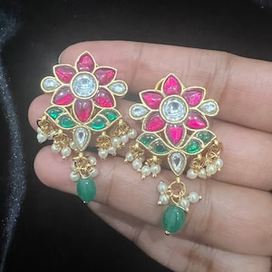 以下が含まれることがあります： 花柄の金色のイヤリングのペア。イヤリングにはピンクとグリーンの石とパールドロップが付いています。