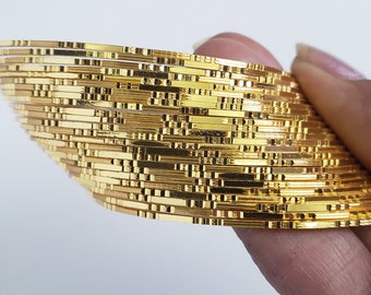 May include: A stack of gold-colored bangles with a textured design. The bangles are stacked in a semi-circle shape.