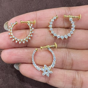 May include: Three gold nose rings with clear rhinestones. The rings are all different styles, one has a star-shaped design, one has a round design, and one has a pointed design.