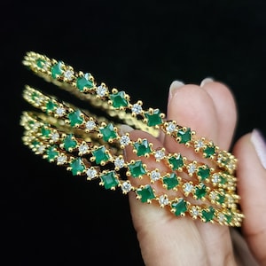 May include: Set of four gold bangles with alternating green and white square-shaped stones.