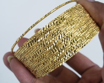 May include: A stack of gold-colored bangles with a textured surface. The bangles are stacked on top of each other and are held in a hand.