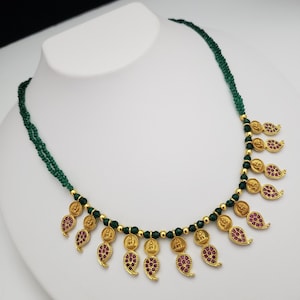 May include: A gold necklace with green beads and dangling paisley-shaped charms with red stones. The charms feature small gold figures.