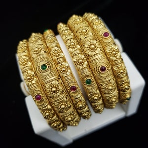 May include: Set of five gold-tone bangles with intricate floral designs and red and green gemstones.