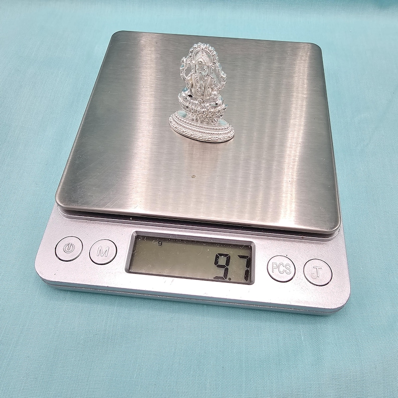 Pu&ograve; includere: Una piccola e ornata statuetta d'argento di una divinit&agrave; &egrave; esposta su una bilancia digitale. La bilancia mostra un peso di 9,7 grammi. La statuetta &egrave; finemente dettagliata e poggia su una base rotonda.