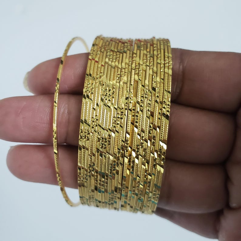 Może przedstawiać: Zestaw 12 złotych bransoletek z fakturowanym wzorem przypominającym diament. Bransoletki są ułożone jedna na drugiej.