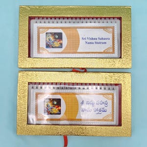 May include: Two silver-framed calendars with gold borders, each containing a colorful illustration and text. The text on the top calendar reads "Sri Vishnu Sahasra Nama Stotram." The calendars are in a gold box with a red ribbon.