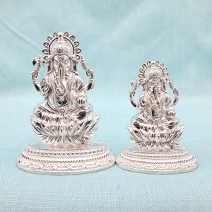 Pu&ograve; includere: Due statue argentate di Ganesha, la divinit&agrave; ind&ugrave;. Sono sedute su basi a forma di fiore di loto con dettagli intricati. La statua pi&ugrave; grande &egrave; alta circa 13 cm, e la pi&ugrave; piccola circa 8 cm.