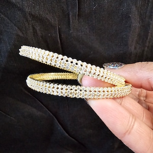 May include: Two gold bangles with a row of clear sparkling stones around each bangle.