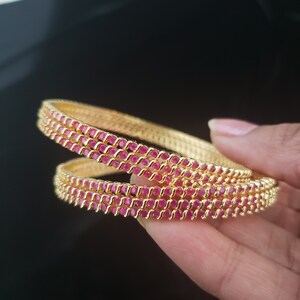 May include: Set of four gold bangles with a row of pink gemstones around each bangle.