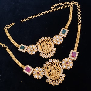 May include: A gold necklace with a chain and two pendants. The pendants are decorated with white stones, green and red stones, and a gold figure.