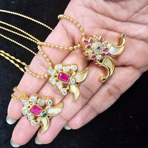 May include: Three gold necklaces with pendants featuring a white shell design, pink and green gemstones, and white cubic zirconia stones.
