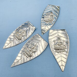 Peut inclure: Quatre pendentifs en argent en forme de feuille avec des motifs complexes représentant une figure de divinité au centre. Chaque pendentif a une surface texturée et une pointe pointue.
