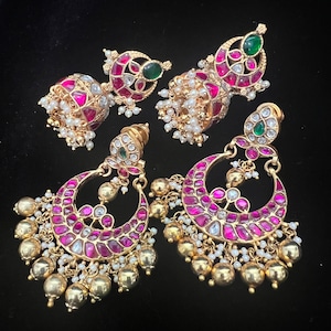 May include: A pair of gold earrings with pink and green stones, pearl accents, and dangling charms. The earrings are in the shape of a crescent moon.