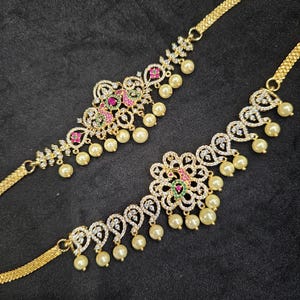 May include: Two gold-tone peacock-shaped waist chains with white pearl accents and colorful gemstones. The chains are adorned with intricate designs and are perfect for adding a touch of elegance to any outfit.