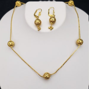 May include: A gold necklace with five round, ornate beads and matching earrings. The beads have a filigree design and are accented with small red gemstones.
