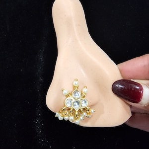 Puede incluir: Anillo de nariz de oro con detalles de perlas blancas y piedras transparentes. El anillo de nariz es una pieza de joyería tradicional de estilo indio.