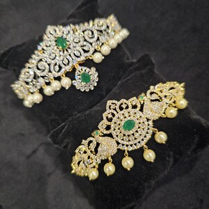 May include: Two gold-tone choker necklaces with white stones and green accents. The necklaces have pearl drop accents.