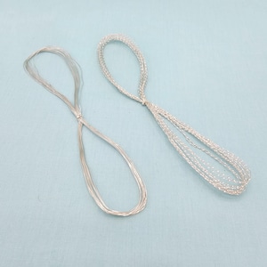 May include: Two silver wire loops, each with a knotted center, rest on a light blue surface. The loops are made of multiple strands of thin, shiny wire, creating a delicate and intricate design. The overall aesthetic is minimalist and elegant.