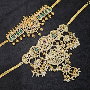 May include: Two gold necklaces with intricate designs and green and white stones. The necklaces have a chain and a pendant with multiple layers of pearls and stones.