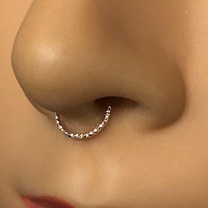 May include: A close-up of a nose piercing with a gold, diamond-shaped hoop.