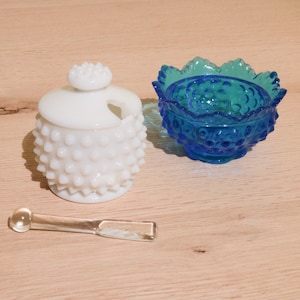 May include: A white milk glass jar with a knob lid and a blue milk glass bowl with a scalloped edge. Both pieces have a textured, bumpy surface.